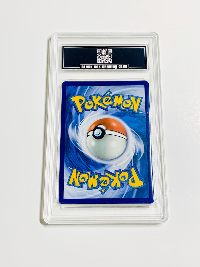 May include: A graded Pok&eacute;mon trading card encased in a clear plastic holder. The card's back features a blue background with the Pok&eacute;mon logo and a Pok&eacute; Ball design. The holder has a black label with the text "BLACK BOX GRADING CLUB".