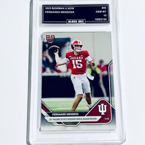 May include: A sports trading card featuring Fernando Mendoza in a red Indiana Hoosiers uniform throwing a football. The card is encased in a protective holder and includes text: "2025 Bowman U Now," "#45," and "30th Passing TD Sets Hoosiers Single-Season Record."