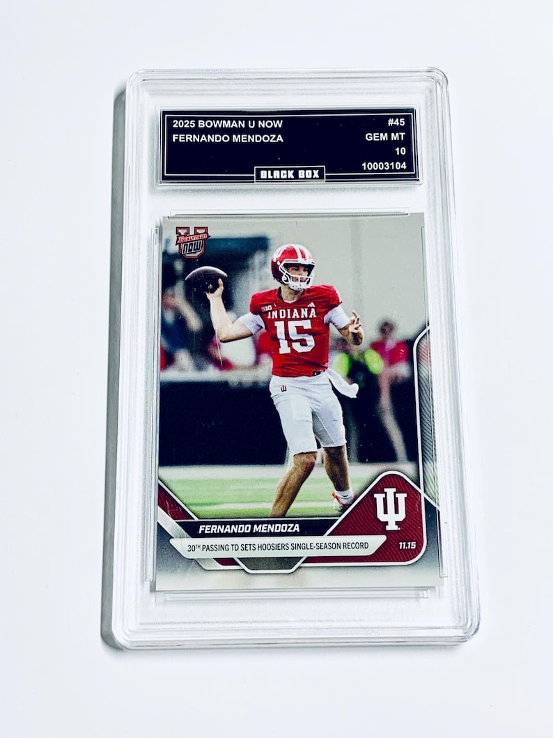 May include: A sports trading card featuring Fernando Mendoza in a red Indiana Hoosiers uniform throwing a football. The card is encased in a protective holder and includes text: "2025 Bowman U Now," "#45," and "30th Passing TD Sets Hoosiers Single-Season Record."