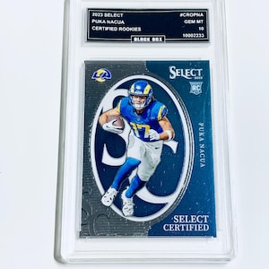 May include: A graded trading card featuring Puka Nacua in a blue and yellow uniform. The card is labeled "2023 Select Certified Rookies" and is encased in a protective holder. The card has the text "SELECT CERTIFIED" and "PUKA NACUA".