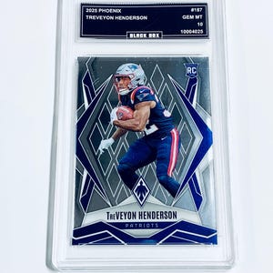 May include: A graded sports trading card featuring Treveyon Henderson of the Patriots. The card is from the 2025 Phoenix series and is graded GEM MT 10. The card has a silver and blue design with the player in action. The card is encased in a clear protective holder.