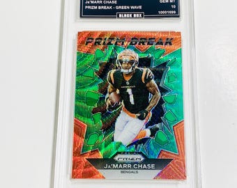 May include: A graded Ja'Marr Chase football card from the 2023 Prizm series. The card features a player in a Bengals uniform against a green and orange background. The card is labeled "Prizm Break - Green Wave" and is encased in a protective holder.