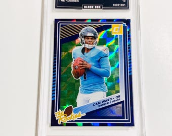 May include: A 2025 Donruss Cam Ward football card, graded GEM MT 10, encased in a protective holder. The card features a player in a light blue uniform, holding a football. The card is labeled "The Rookies" and "Tennessee Titans".