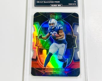 May include: A Jonathan Taylor football card from the 2022 Select series. The card is a die-cut Black/Red Prizm, graded GEM MT 10. The card features a player in a Colts uniform. The card is encased in a protective holder.