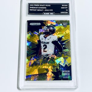 May include: A football trading card encased in a clear plastic holder. The card features a player in a white and black uniform with the number 2. The card has gold and yellow accents with the text "INSTANT IMPACT". The top of the holder has text that reads "2025 Prizm Draft Picks".