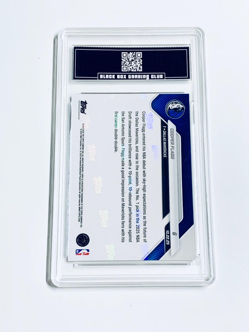 Puede incluir: Una tarjeta de baloncesto de Cooper Flagg calificada en un estuche protector transparente. La tarjeta presenta el logotipo de los Dallas Mavericks y la informaci&oacute;n del jugador. El estuche tiene una etiqueta negra con el texto "BLACK BOX GRADING CLUB".