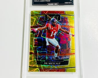 May include: A DK Metcalf football trading card from the 2022 Select Draft Picks series. The card is graded GEM MT 10 and features a gold lazer prizm design. The card is encased in a protective holder.