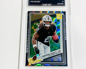May include: A football trading card featuring Ashton Jeanty of the Las Vegas Raiders. The card is encased in a protective holder and includes the text "2025 Donruss," "The Rookies," and "Black Box."