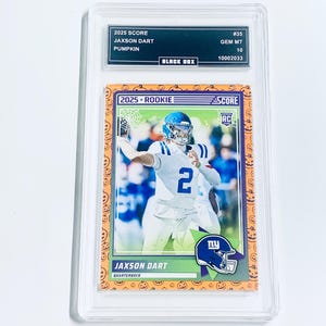 May include: A graded 2025 Score Jaxson Dart Pumpkin rookie football card. The card features a player in a blue and white uniform. The card is graded GEM MT 10 by Black Box. The card has a Halloween-themed border with pumpkins.