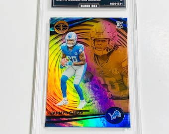May include: A Jahmyr Gibbs football trading card from the 2023 Illusions Trophy Collection Orange set. The card is graded GEM MT 10 and features a vibrant image of the player in action. The card is encased in a protective holder.