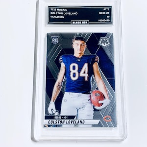 May include: A white ceramic mug with a black handle and the text "But First, Coffee" in a bold, black font. The mug is set against a blurred background, suggesting a cozy setting.