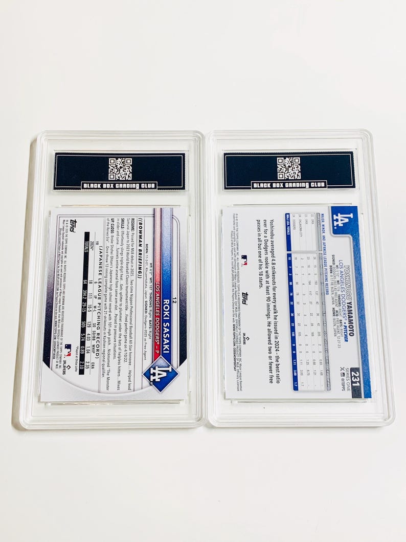 May include: Two baseball trading cards in protective cases. One card features Roki Sasaki of the Los Angeles Dodgers. The other card features Yoshinobu Yamamoto, also of the Los Angeles Dodgers. Both cards are graded by Black Box Grading Club.