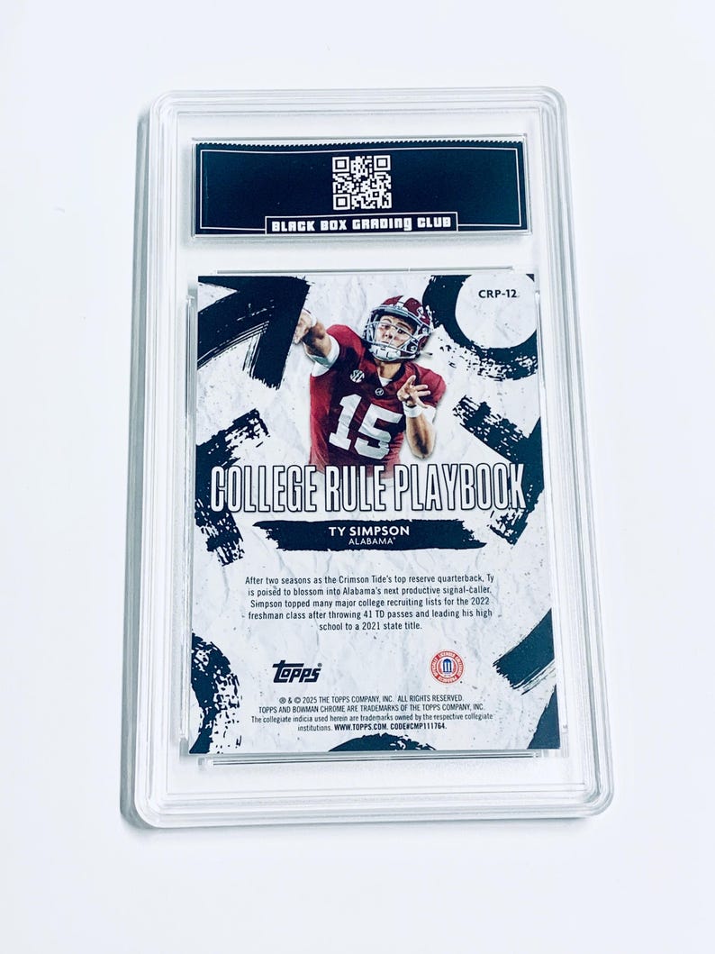 Op de afbeelding: Een voetbal trading card in een doorzichtige plastic hoes. De kaart toont een speler in een karmozijnrood shirt met nummer 15. Tekst bevat "COLLEGE RULE PLAYBOOK" en "TY SIMPSON ALABAMA". De bovenkant heeft een zwart label met "BLACK BOX GRADING CLUB".