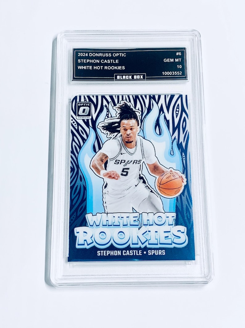 Może przedstawiać: Oceniona karta do koszyk&oacute;wki Donruss Optic 2024 z Stephonem Castle z Spurs. Karta oznaczona jest jako "White Hot Rookies" z niebiesko-białym wzorem płomienia. Karta jest zamknięta w przezroczystym uchwycie ochronnym.