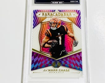 May include: A graded trading card featuring Ja'Marr Chase in a Bengals uniform. The card is from the 2024 Illusions set, titled "Abracadabra." The card has a colorful design with the player's name and team logo visible.
