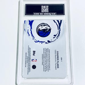 Puede incluir: Una tarjeta de baloncesto de Cooper Flagg de los Dallas Mavericks, calificada y protegida en una funda transparente. La tarjeta muestra el logotipo de los Mavericks y el texto "COOPER FLAGG" y "Dallas Mavericks | Forward". Calificada por Black Box Grading Club.