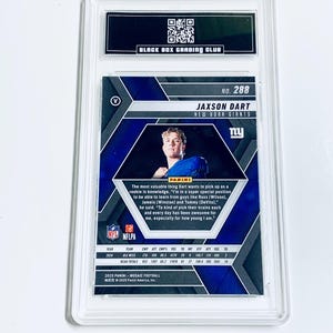Puede incluir: Una tarjeta de f&uacute;tbol Jaxson Dart de los New York Giants calificada. La tarjeta presenta una foto del jugador y estad&iacute;sticas. La tarjeta est&aacute; encerrada en un soporte de pl&aacute;stico transparente con una etiqueta en blanco y negro de Black Box Grading Club.