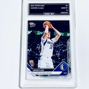Puede incluir: Una tarjeta de baloncesto Cooper Flagg 2025 Topps Now calificada. La tarjeta presenta a un jugador con uniforme blanco y azul lanzando un bal&oacute;n de baloncesto. La tarjeta est&aacute; dentro de un soporte de pl&aacute;stico transparente con el texto "2025 Topps Now" y "Cooper Flagg".