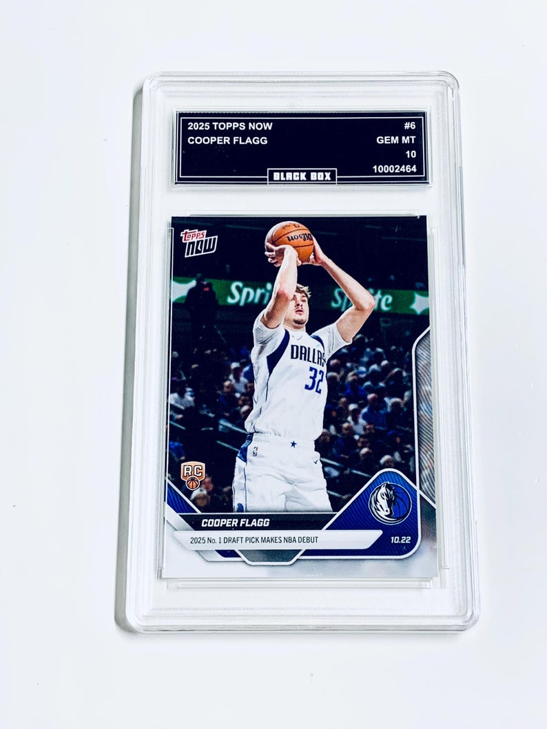 Puede incluir: Una tarjeta de baloncesto Cooper Flagg 2025 Topps Now calificada. La tarjeta presenta a un jugador con uniforme blanco y azul lanzando un bal&oacute;n de baloncesto. La tarjeta est&aacute; dentro de un soporte de pl&aacute;stico transparente con el texto "2025 Topps Now" y "Cooper Flagg".
