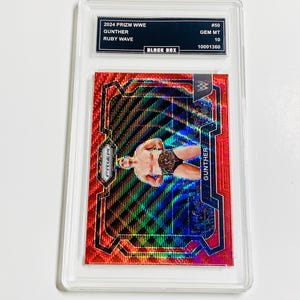 Könnte beinhalten: Eine 2024 Prizm WWE Sammelkarte mit Gunther im Ruby Wave Design, in einer Schutzhülle. Der Text zeigt "GEM MT 10". Die Karte hat ein rot-schwarzes Farbschema und zeigt das Bild des Wrestlers.