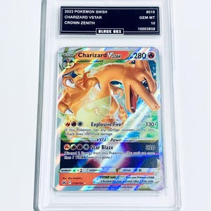 May include: A graded Pokémon Charizard VSTAR card from the Crown Zenith set, in a protective case. The card shows a fiery Charizard illustration and details about its attacks. The card is in a protective case.
