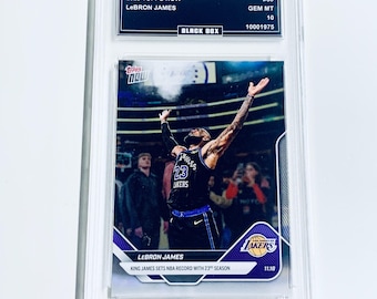 Op de afbeelding: Een beoordeelde 2025 Topps Now LeBron James trading card. De kaart toont LeBron James in een Lakers-uniform, die een record viert. De kaart is ingesloten in een heldere beschermhoes met de tekst "BLACK BOX" en "GEM MT 10".