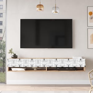 May include: A black television mounted on a white wall above a wooden entertainment center with a black and white geometric pattern on the front. Two gold pendant lights hang above the television.