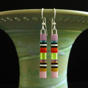 May include: A pair of colorful, rectangular earrings with a vertical striped design. The earrings feature a combination of pink, purple, green, orange, black, and white blocks. The earrings hang from silver hooks.