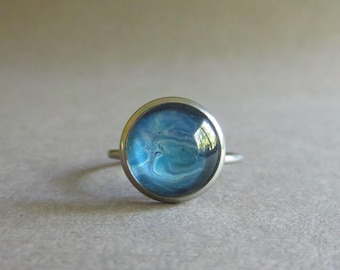 Pale blue adjustable stainless steel fluid art fun ring. Flow art ring. Poured paint ring. Blue cabochon fun ring. Stainless steel ring.