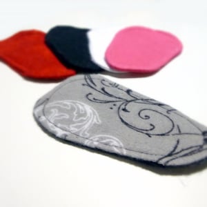 May include: Five fabric scraps in various colors and patterns. The scraps are shaped like rounded rectangles. The scraps are red, white, black, pink, and gray with a black and white floral pattern.