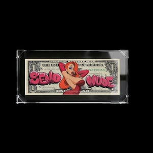 May include: Framed one-dollar bill featuring a cartoon woman in a red dress and the words "SEND NUDE" in pink graffiti-style lettering. The bill is encased in a clear acrylic frame.