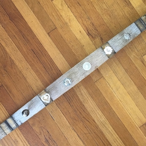 May include: A long, weathered piece of wood with five metal accents. The accents are in the shape of a heart, a circle, and three different flowers. The wood is light brown and has a rustic look.