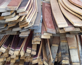 May include: A pile of wooden barrel staves, some are stained red, some are natural wood color, and some are dark brown. The staves are stacked in a random pattern.
