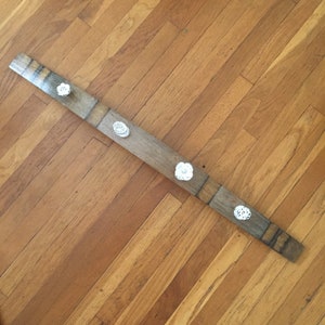 May include: A wooden coat rack made from a reclaimed wine barrel stave with four white porcelain knobs.