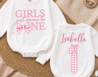 May include: Two white long-sleeved baby rompers. The first features the pink text "GIRLS just wanna be ONE" with a pink gingham bow. The second features the name "Isabella" in pink script above a large pink gingham number one with a bow.