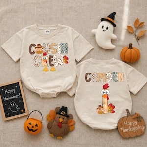 May include: Two beige short-sleeved rompers featuring Thanksgiving-themed graphics. One displays the text "COUSIN CREW" with a turkey illustration, while the other shows the name "CAMDEN" with a turkey and the number one. Includes a ghost plush, a pumpkin, a turkey plush, a jack-o'-lantern bucket, and two small signs reading "Happy Halloween" and "Happy Thanksgiving."