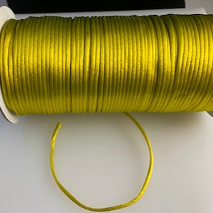 May include: A spool of bright yellow satin cord. The cord is wound tightly around the spool and a length of cord is hanging off the spool.