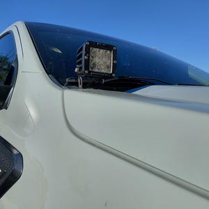 Könnte beinhalten: Nahaufnahme eines weißen Lastwagens mit einer schwarzen LED-Lichtleiste, die über der Windschutzscheibe montiert ist. Der Lastwagen hat einen schwarzen Seitenspiegel und ein schwarzes Emblem mit der Aufschrift "RANGER XLT". Der Himmel ist blau.