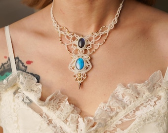 May include: Cream-colored macrame necklace featuring a central pendant with a blue and a purple gemstone. The necklace has gold-colored bead accents and a delicate, lacy design. The necklace is worn on a person.