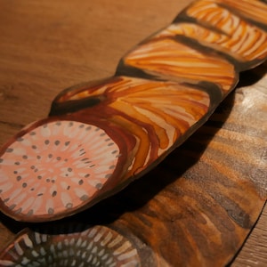 May include: A set of five hand-painted wooden wall art pieces. Each piece features a different abstract design in shades of brown, orange, and pink. The pieces are layered on top of each other, creating a unique and textured look.