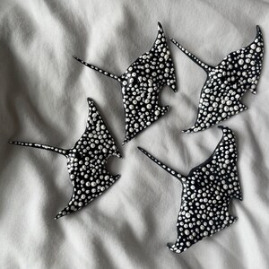 Può includere: Quattro sculture di manta nera con pois bianchi. Le mante sono disposte in un gruppo su uno sfondo di tessuto bianco.