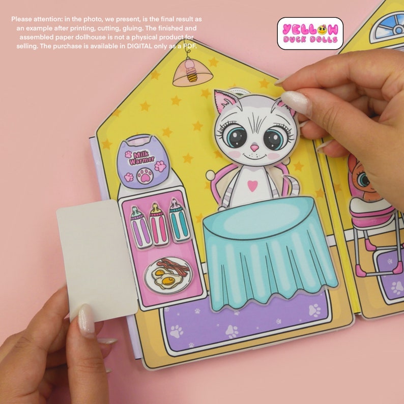 Op de afbeelding: Een printbaar papieren poppenhuis met een gele buitenkant en een roze interieur. Het poppenhuis heeft een poppenkat, een tafel, een melkwarmer en een kinderstoel. Het poppenhuis is onderdeel van een set met printbare papieren poppen en accessoires.