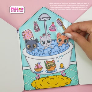 Op de afbeelding: Een printbaar papieren poppenhuis met een blauw en groen badkamerinterieur. Het poppenhuis heeft een badkuip met drie katten erin, een douche, een fles badschuim, een handdoek en een rubberen eendje. De tekst "BUBBLE BATH" staat op de fles badschuim.