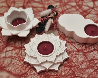 May include: Three white ceramic candle holders with red candles. The holders are shaped like a flower, a cloud, and a mandala.
