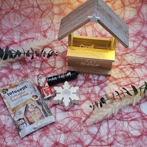 May include: A white snowflake candle holder, a small red and white Santa Claus figurine, a brown paper packet with the text "tetesept. Dein s&uuml;&szlig;er Wintertraum" and a black and white candle with the text "Fr&ouml;hliches Fest!" on a red and white background.