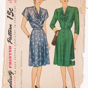 Puede incluir: Patrón Simplicity vintage 1579 con dos diseños de vestidos. Uno es azul con un estampado blanco, el otro verde. El patrón incluye medidas de busto 36 y cadera 39. El texto dice "Simplicity Printed Pattern 15c".