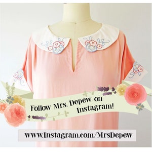 May include: A light pink dress with a white collar and cuffs. The collar and cuffs are embroidered with blue, red, and yellow floral designs. The dress has short sleeves and a v-neck. The image includes the text "Follow Mrs. Depew on Instagram!" and a website address.