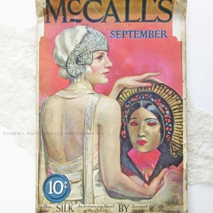 May include: A vintage McCall's magazine cover from September, featuring a woman in a white dress and a beaded headband, holding a mask with a woman's face. The cover text reads "McCall's" and "September" and includes the price "10&cent;".