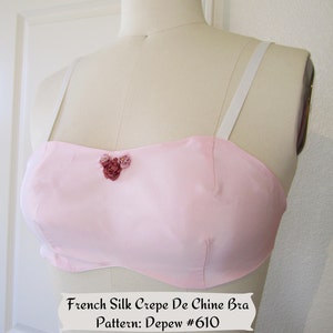 May include: A pink silk crepe de chine bra with white straps and a floral embellishment. French Silk Crepe De Chine Bra Pattern: Depew #610