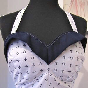 May include: A white halter top with a navy blue trim and a pattern of small anchors. The top is made of a soft, lightweight fabric and has a relaxed fit.